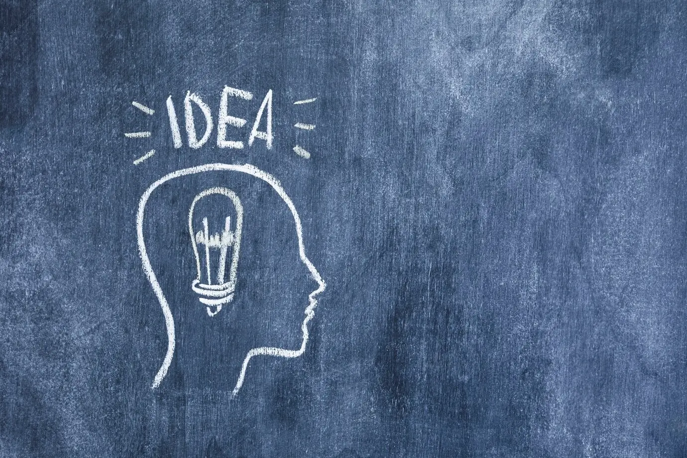 The word “Idea” above an outlined face with a light bulb, drawn on a chalkboard.