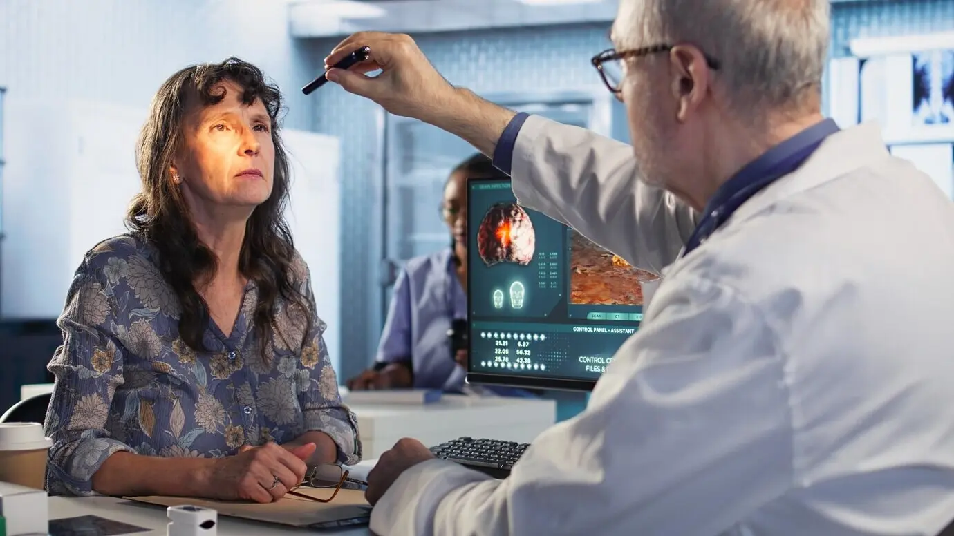 A male healthcare professional performs a concussion test with a penlight in an exam room, evaluating a woman.
