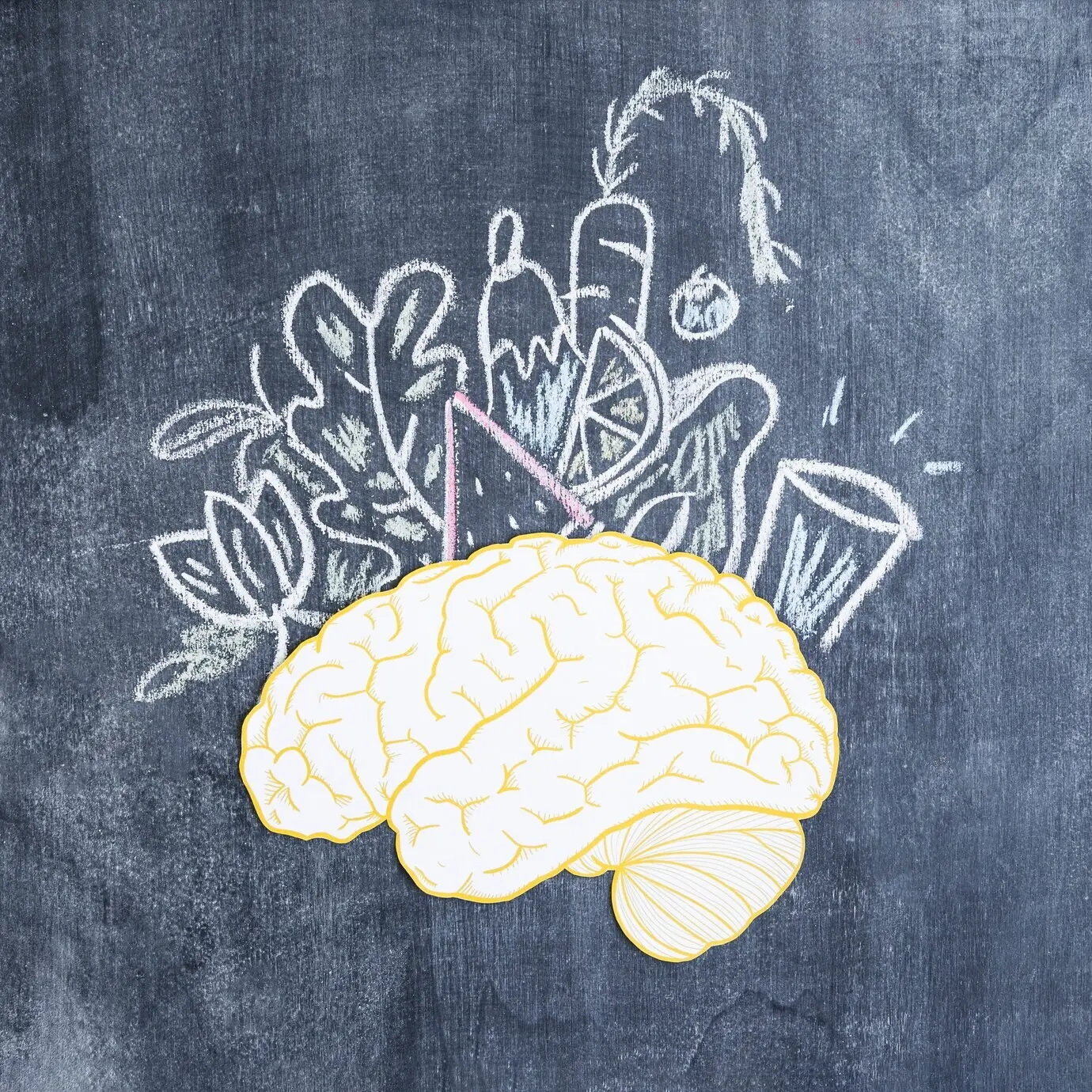 Assorted drawn vegetables over a paper brain cutout on a chalkboard.
